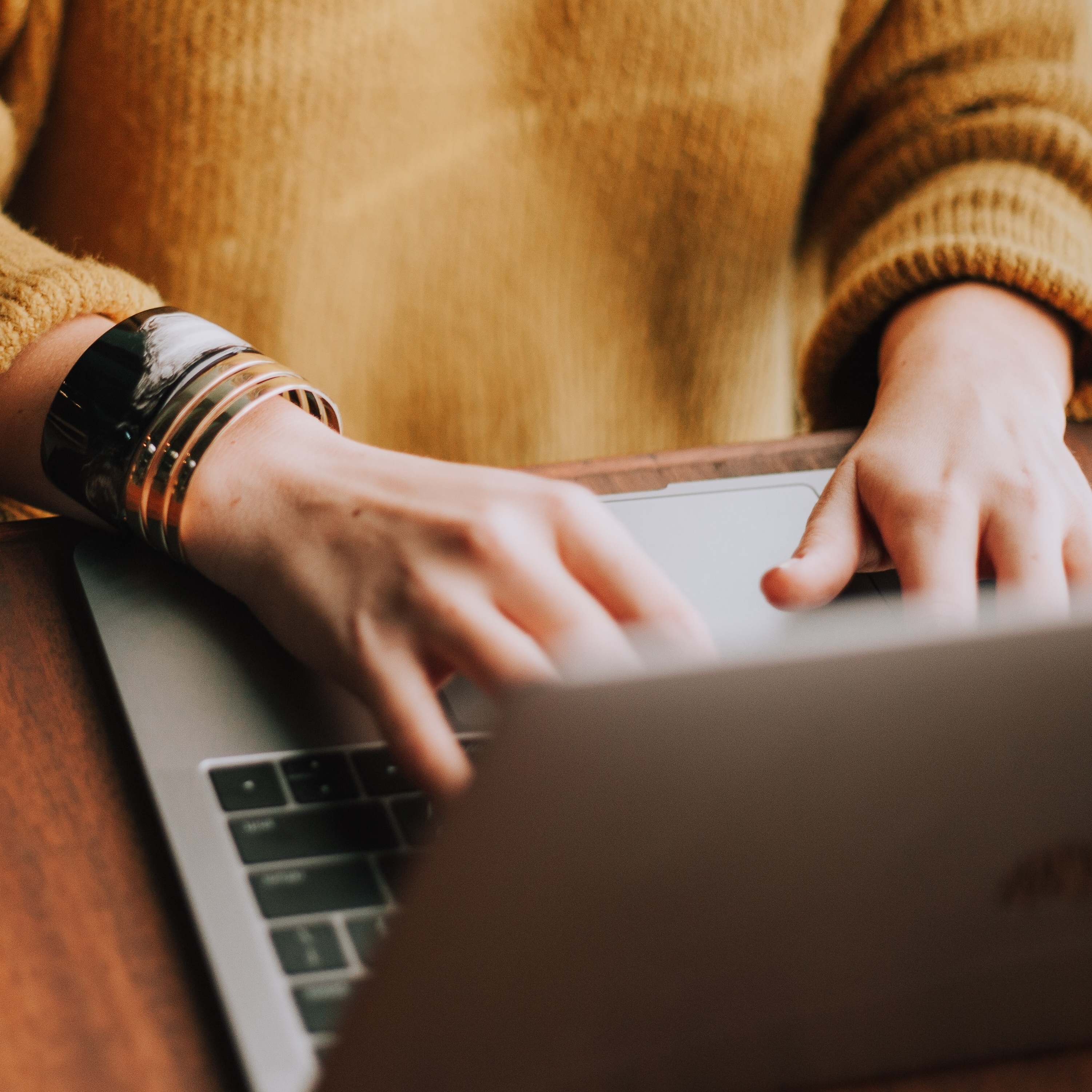 A lady in a mustard sweater typing on a laptop